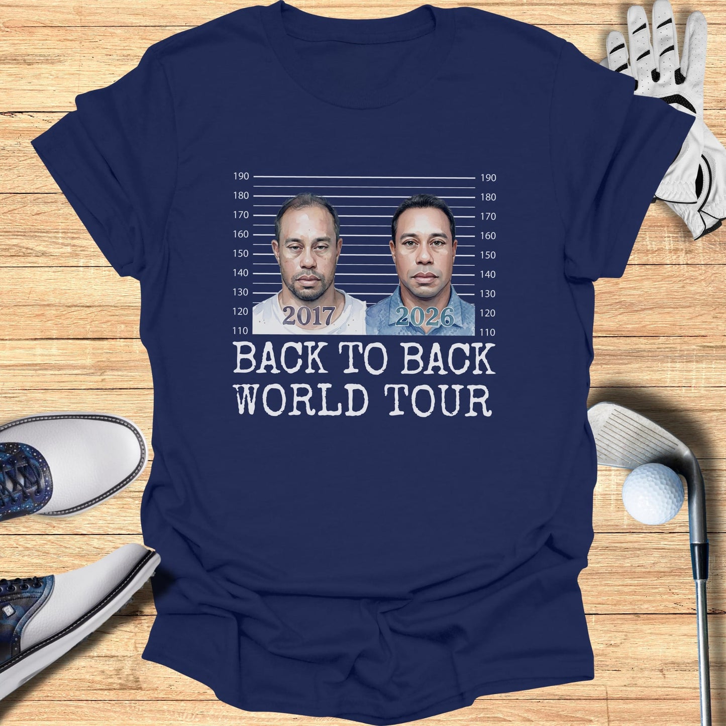 T-shirt graphic with mugshot-style images of Tiger Woods, dated 2017 and 2026, reading "BACK TO BACK WORLD TOUR".
