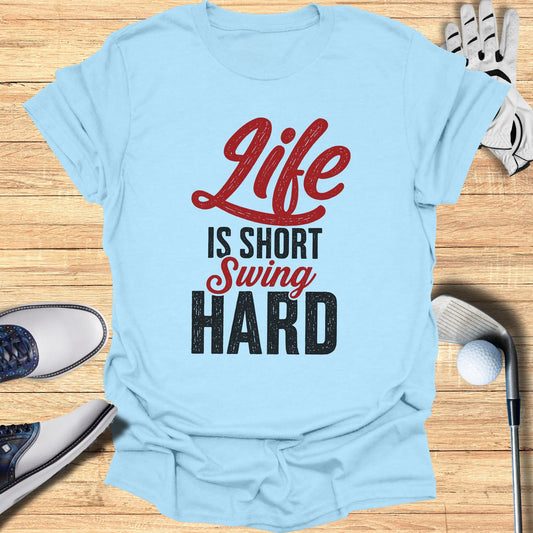 Light blue t-shirt with "Life Is Short Swing Hard" text, surrounded by golf accessories.