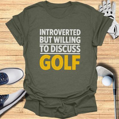 T-shirt with "Introverted but willing to discuss GOLF" text, on a wooden background with golf shoes and ball.