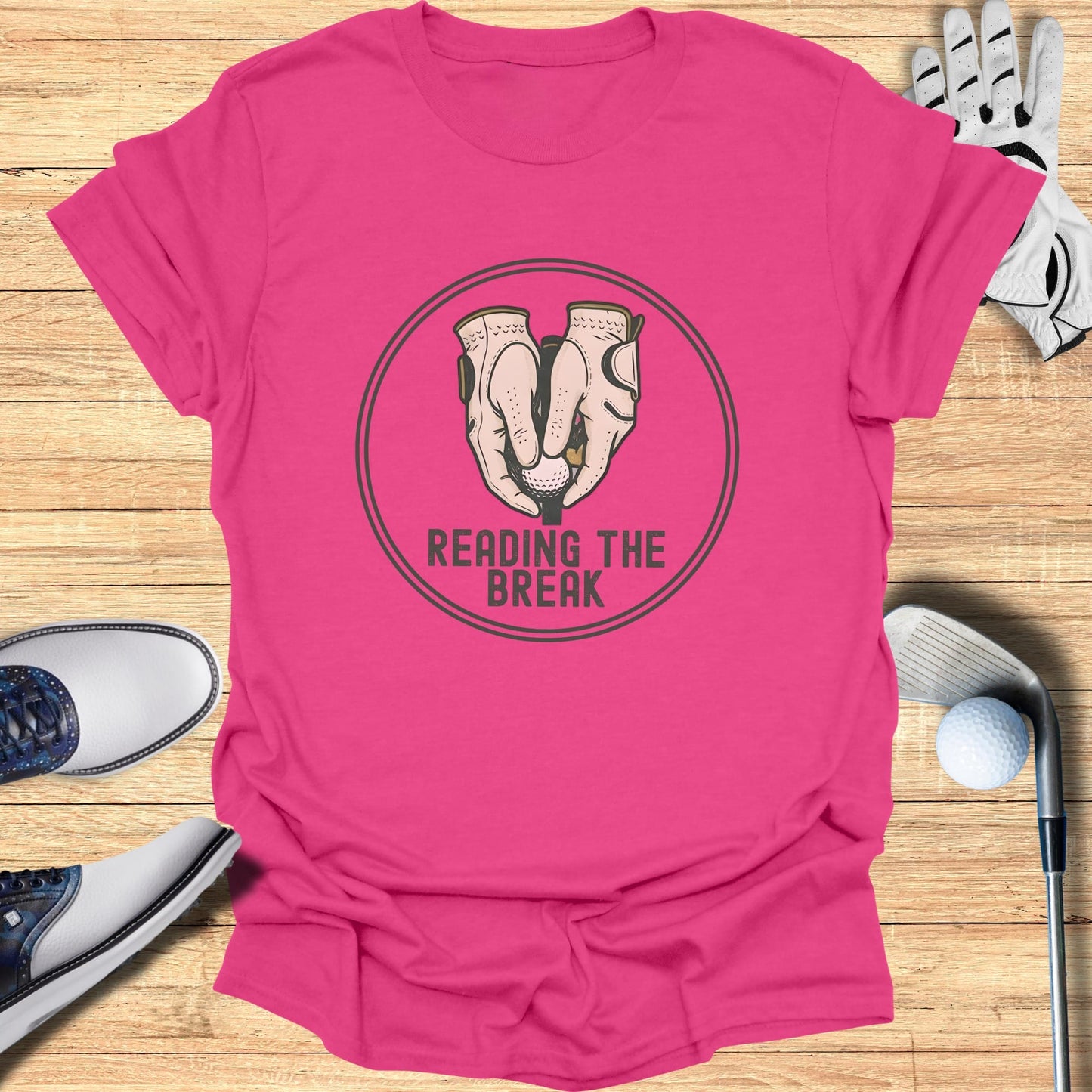 Pink t-shirt with "Reading the Break" golf graphic, golf shoes, glove, and ball.