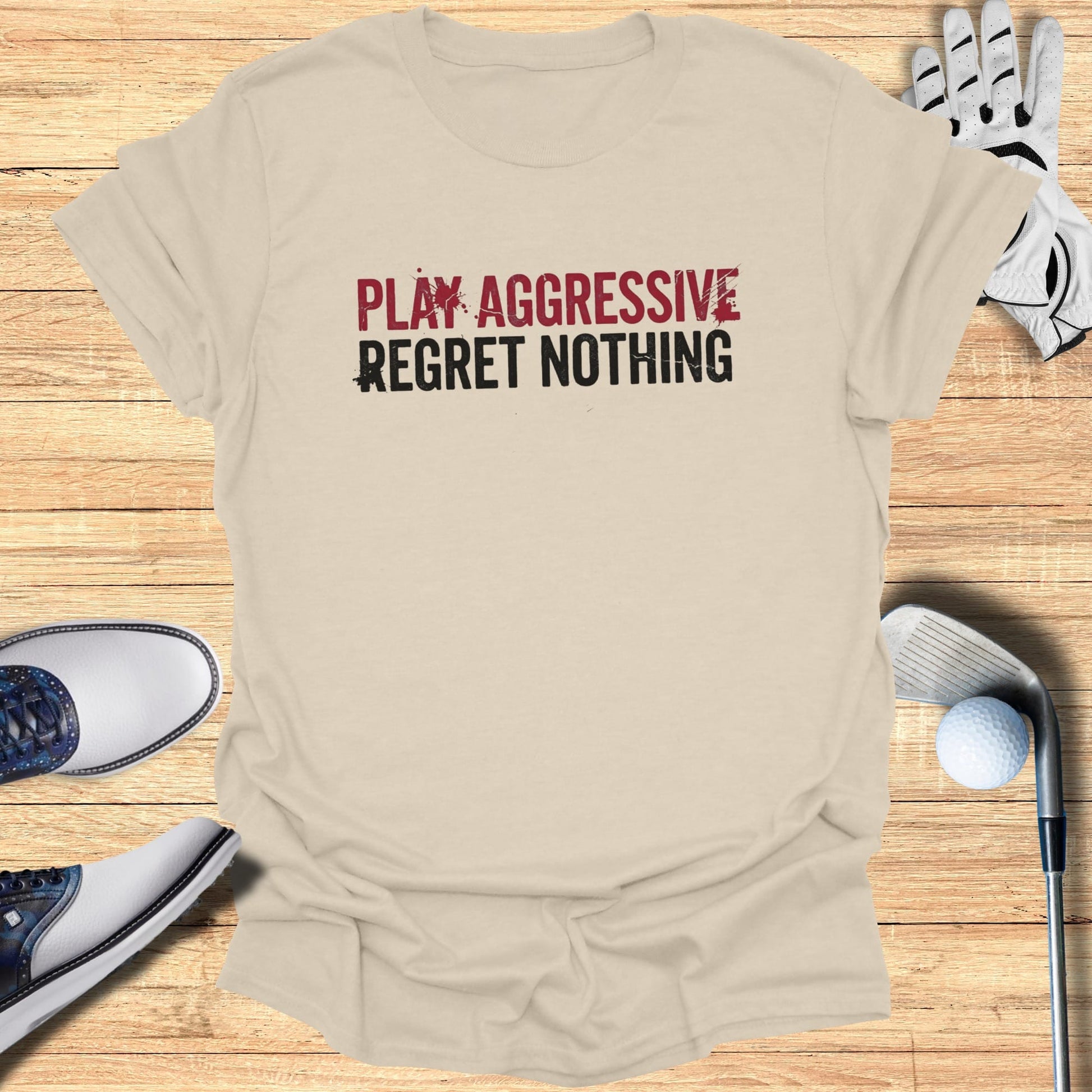 Tan t-shirt with "PLAY AGGRESSIVE REGRET NOTHING" text and golf accessories.