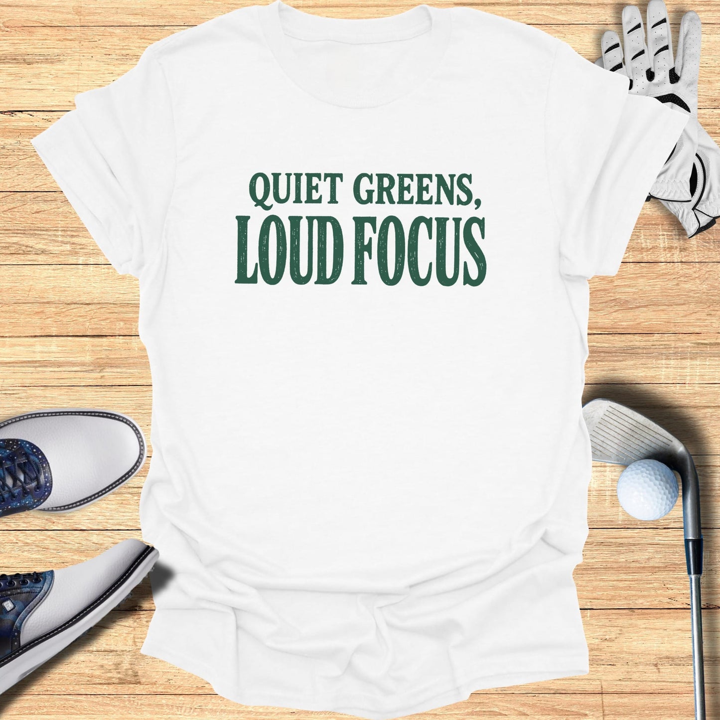 White t-shirt with "QUIET GREENS, LOUD FOCUS" text, golf accessories.