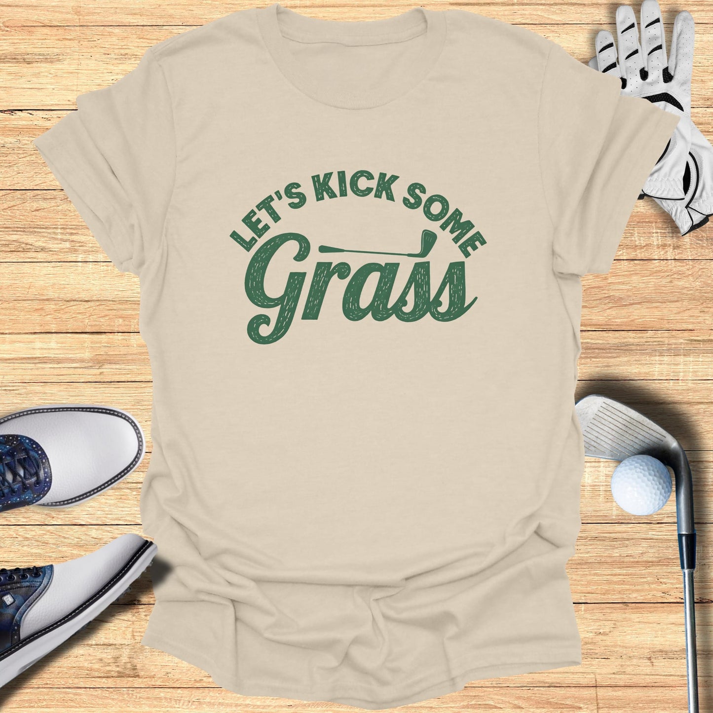 Tan t-shirt with "Let's Kick Some Grass" text, golf shoes, and clubs.