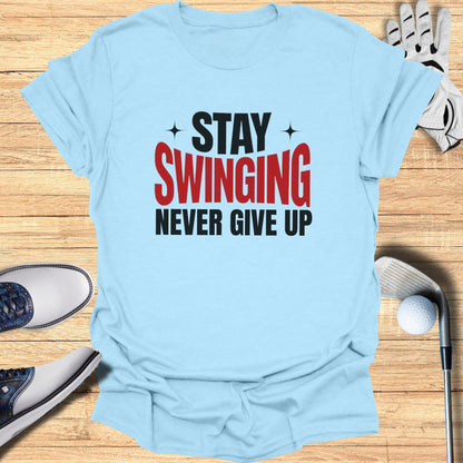 Light blue t-shirt with "STAY SWINGING NEVER GIVE UP" text, golf club, glove, and shoes.