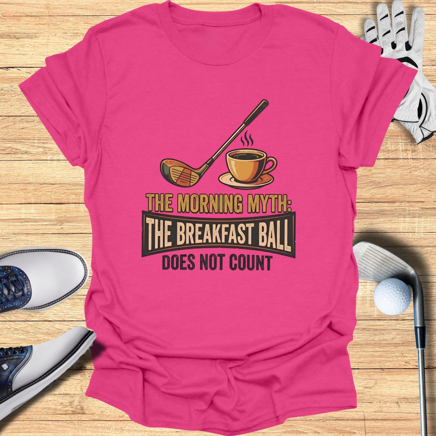 Pink t-shirt with "The Morning Myth: The Breakfast Ball Does Not Count" text and golf illustration.
