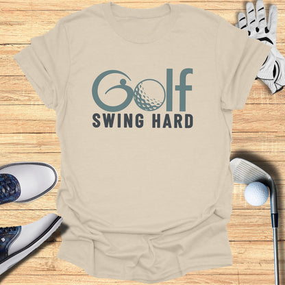 Cream t-shirt with "Golf Swing Hard" text and golf equipment on wooden surface.