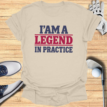 T-shirt with text "I'm a Legend in Practice" on a wooden surface with golf accessories.