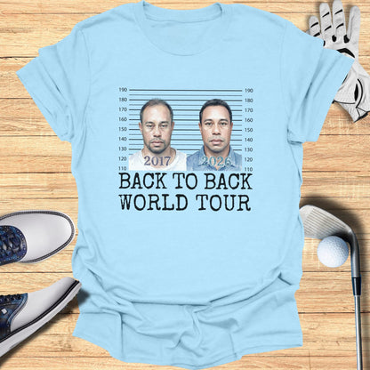 Light blue t-shirt with mugshot-style images of Tiger Woods from 2017 and 2026, text reads "BACK TO BACK WORLD TOUR".