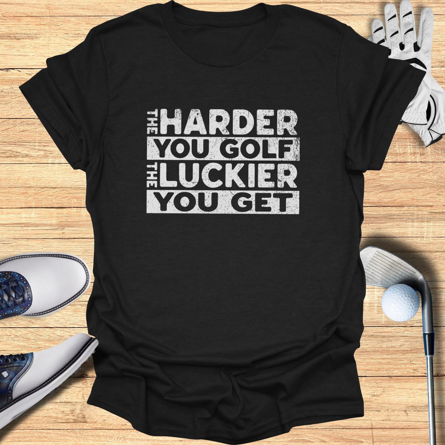 Black t-shirt with white text "THE HARDER YOU GOLF THE LUCKIER YOU GET".