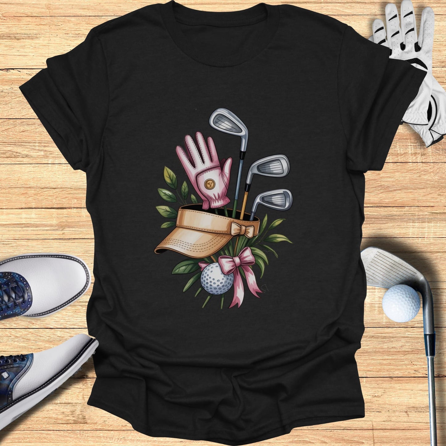 Golf clubs, visor, glove, ball, and pink ribbon on black t-shirt.