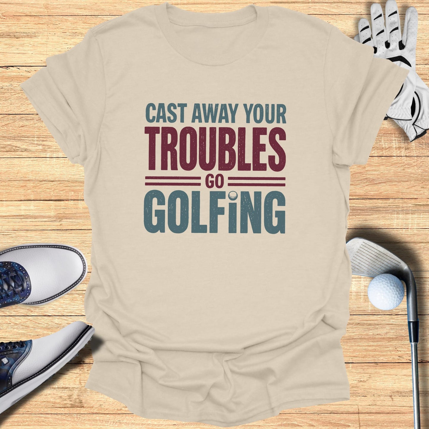 Beige t-shirt with "Cast Away Your Troubles Go Golfing" text, golf shoes, glove, and club.