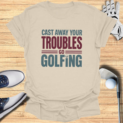 Beige t-shirt with "Cast Away Your Troubles Go Golfing" text, golf shoes, glove, and club.