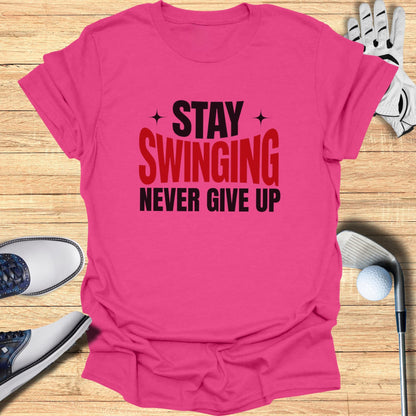 Pink t-shirt with "Stay Swinging Never Give Up" text, golf clubs, shoes, and ball.