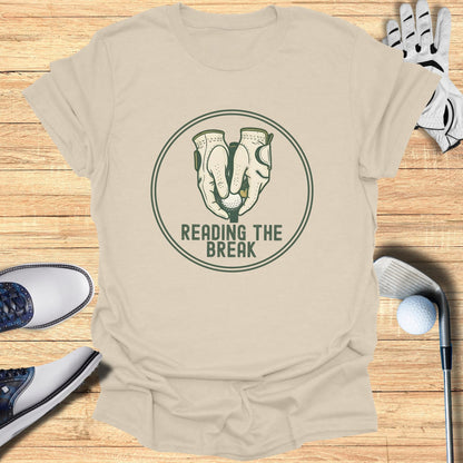Golf gloves and balls on a beige t-shirt with "READING THE BREAK" text.