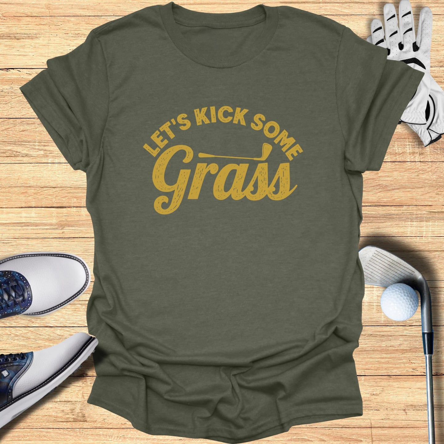 Olive green t-shirt with "Let's Kick Some Grass" text, golf accessories.