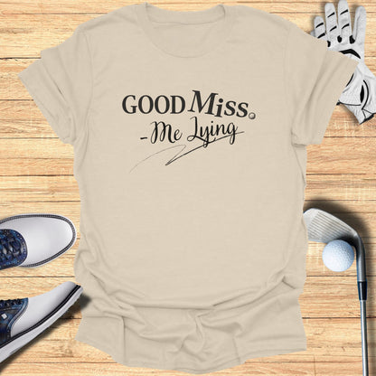 Light tan t-shirt with "Good Miss -Me Lying" text, golf accessories.