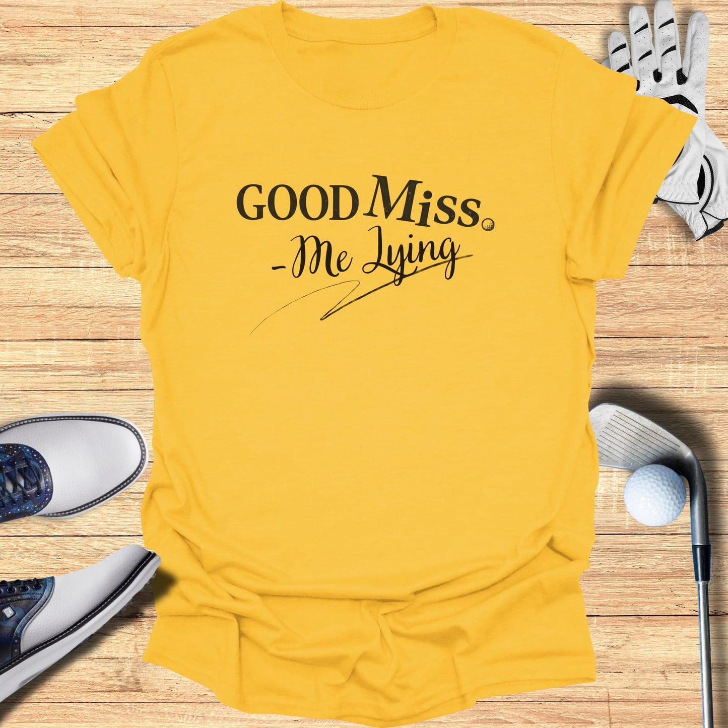 Yellow t-shirt with "Good Miss. -Me Lying." text, golf accessories.