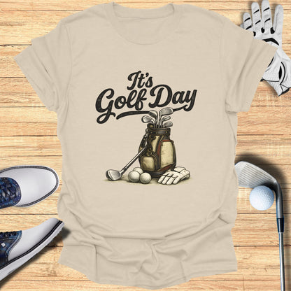 Light beige t-shirt with "It's Golf Day" text and golf bag with clubs and balls.