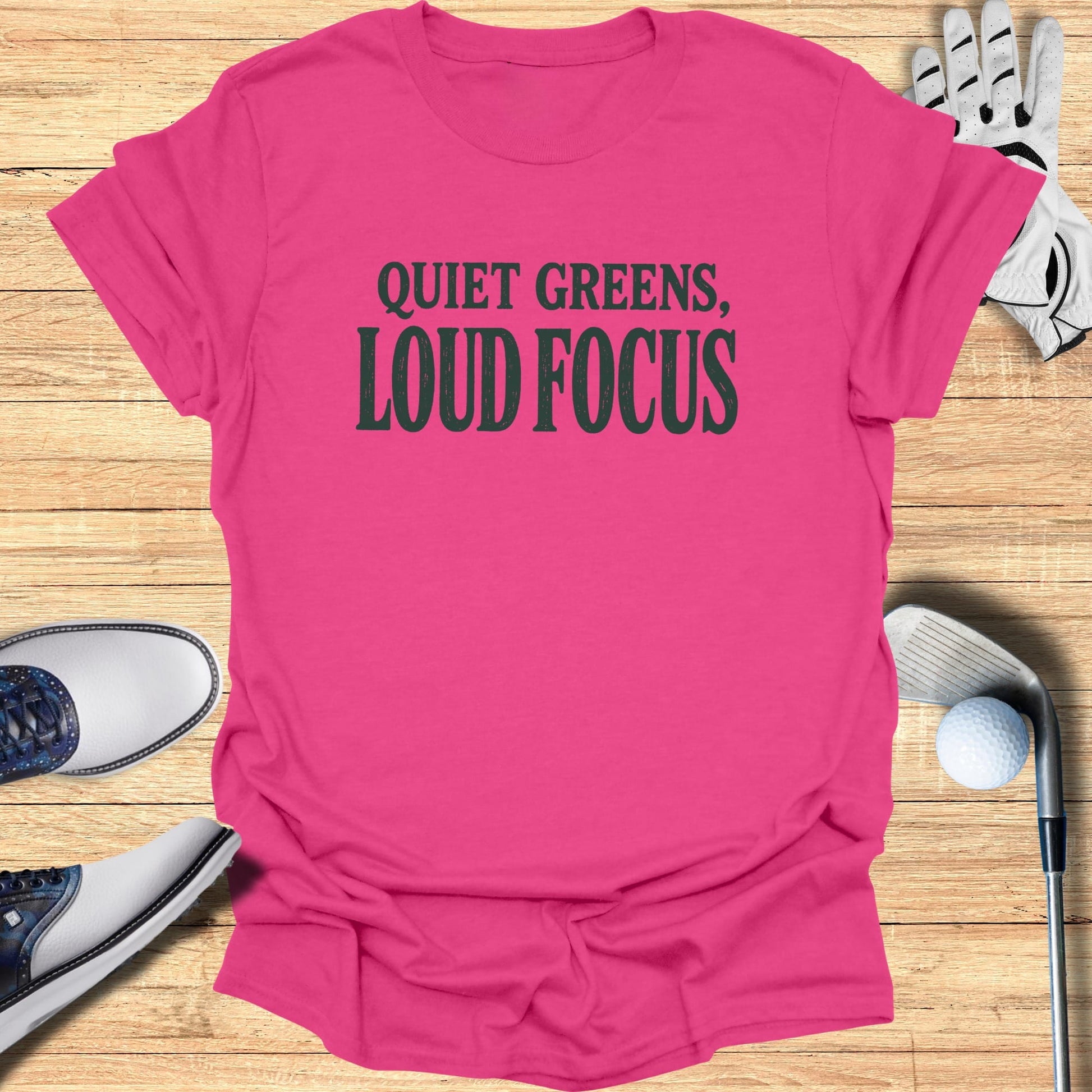Pink t-shirt with "Quiet Greens, Loud Focus" graphic, alongside golf shoes and club.