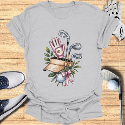 Golf gear illustration on a t-shirt: clubs, ball, glove, visor, and pink bow.