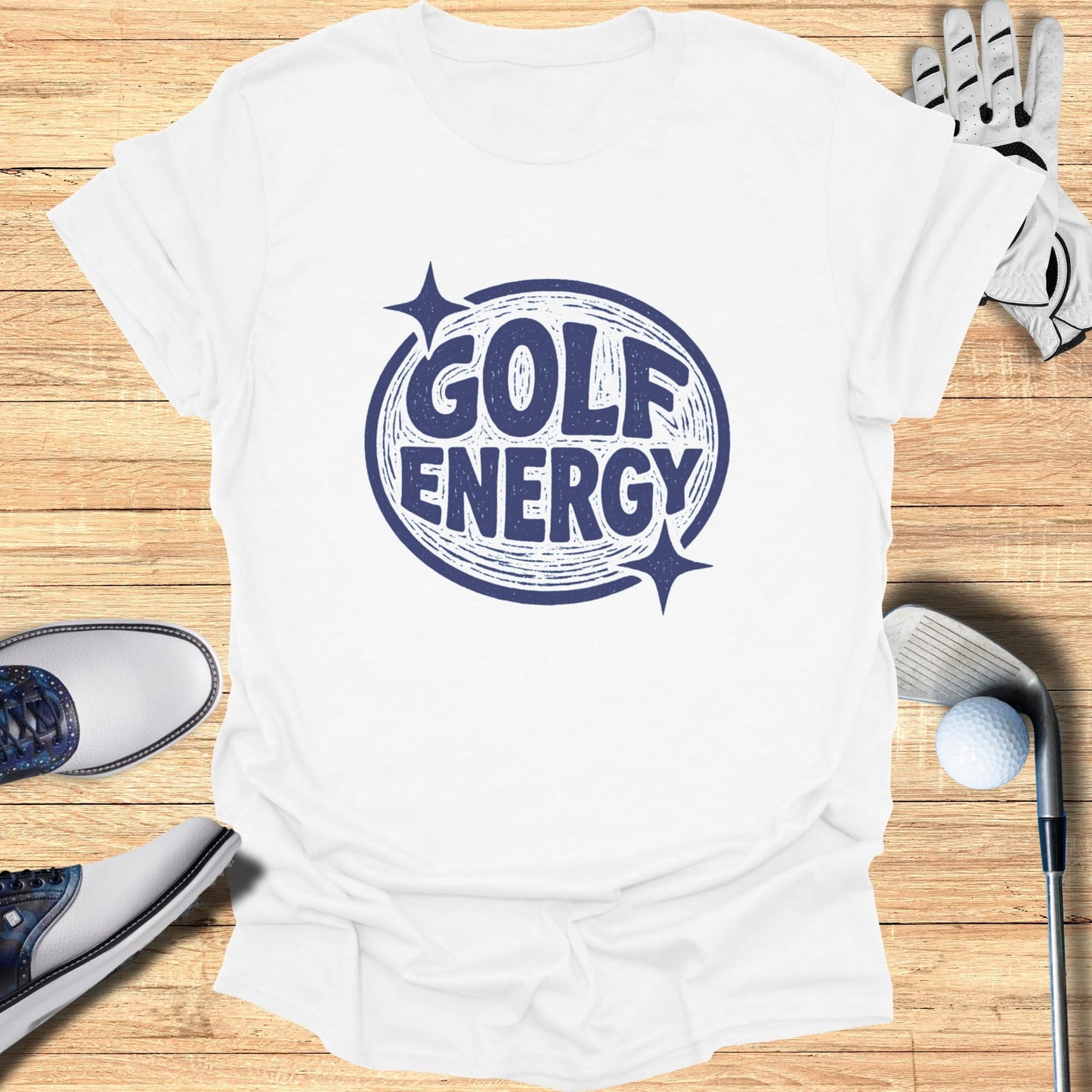 White t-shirt with "GOLF ENERGY" text and sparkles on a wooden background.