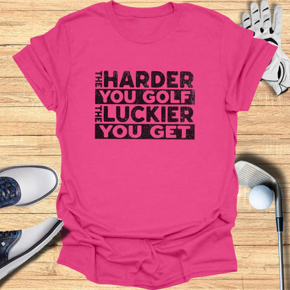 Pink t-shirt with "THE HARDER YOU GOLF THE LUCKIER YOU GET" text.