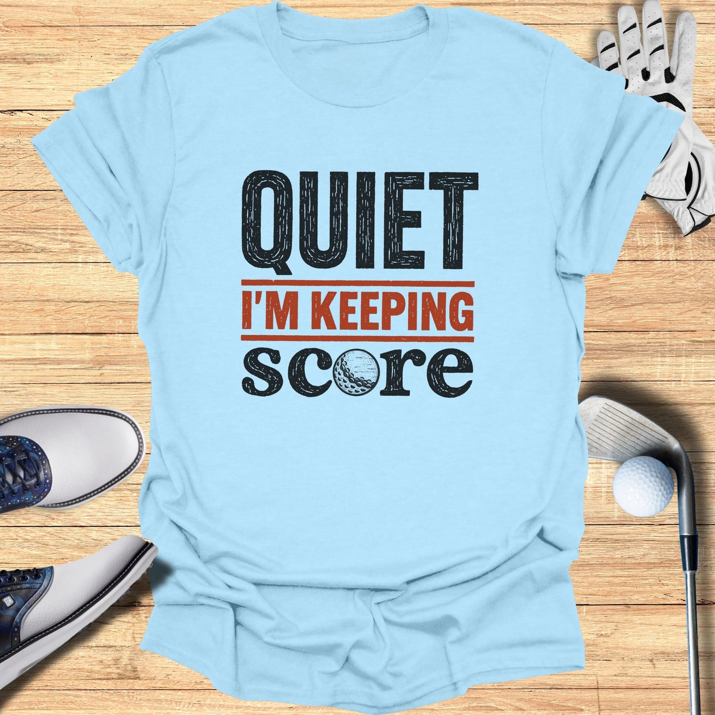 Light blue t-shirt with "QUIET I'M KEEPING SCORE" text and golf accessories.