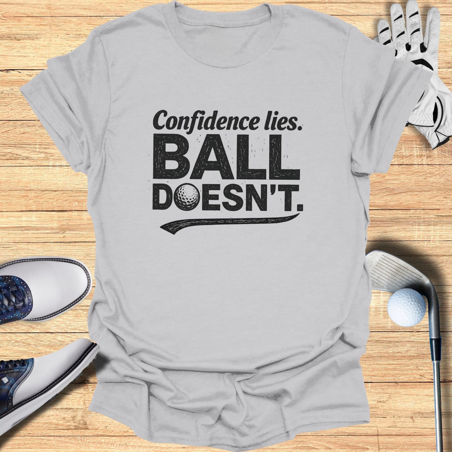 Grey t-shirt with "Confidence lies. BALL DOESN'T." text and golf accessories.