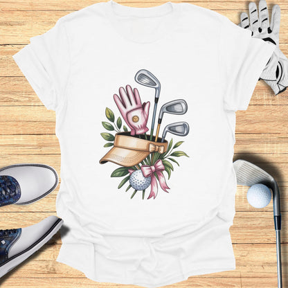 White t-shirt with graphic of golf clubs, ball, glove, and visor with pink bow.